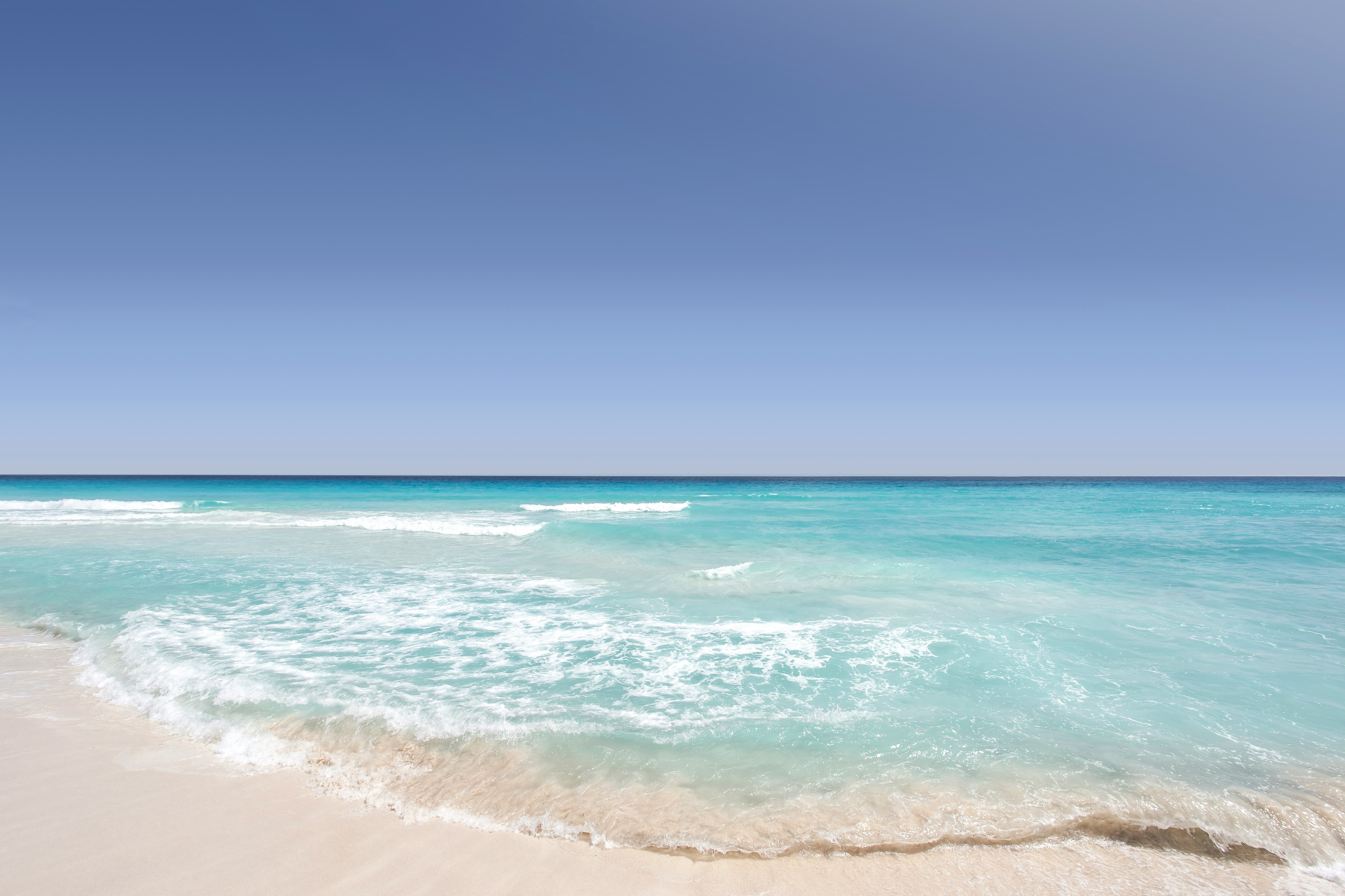 Clear blue ocean washing on the sandy shore on a clear day in Cancún